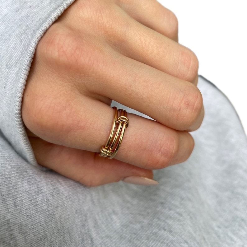 May include: A gold-toned ring with multiple bands twisted together. The ring is worn on a finger.