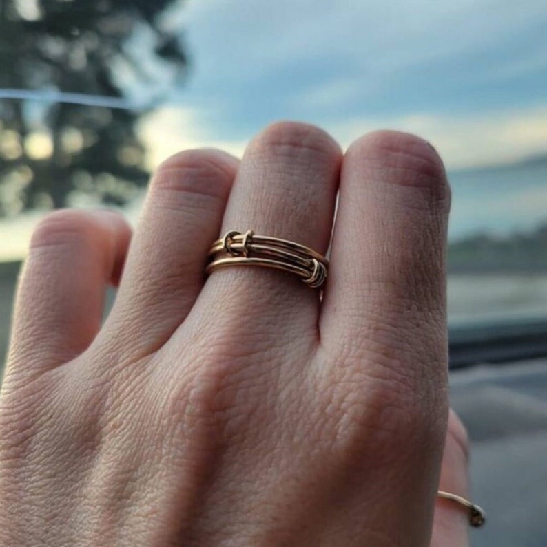 May include: A gold wire ring with multiple bands twisted together. The ring is worn on a finger.