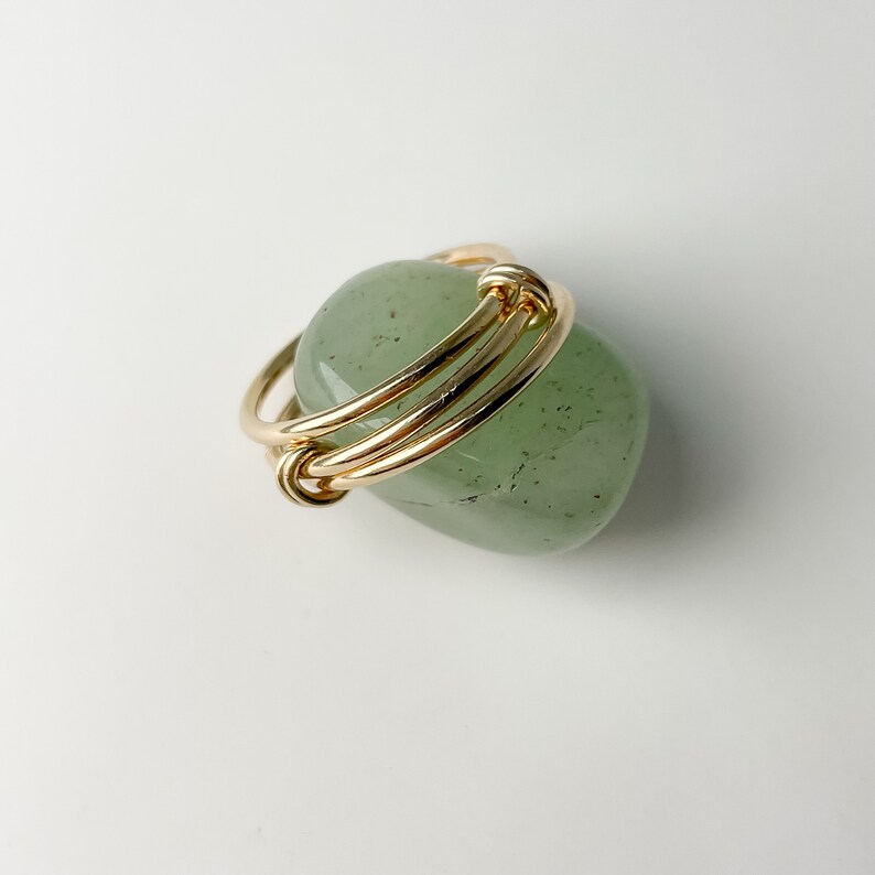 May include: A green stone ring with a gold wire wrapped around it.