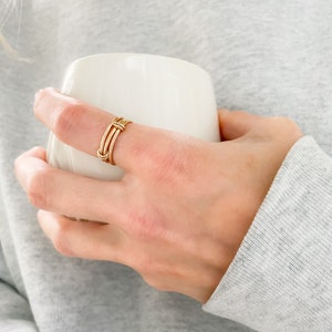 May include: A gold ring with a woven design. The ring is worn on a person's finger.