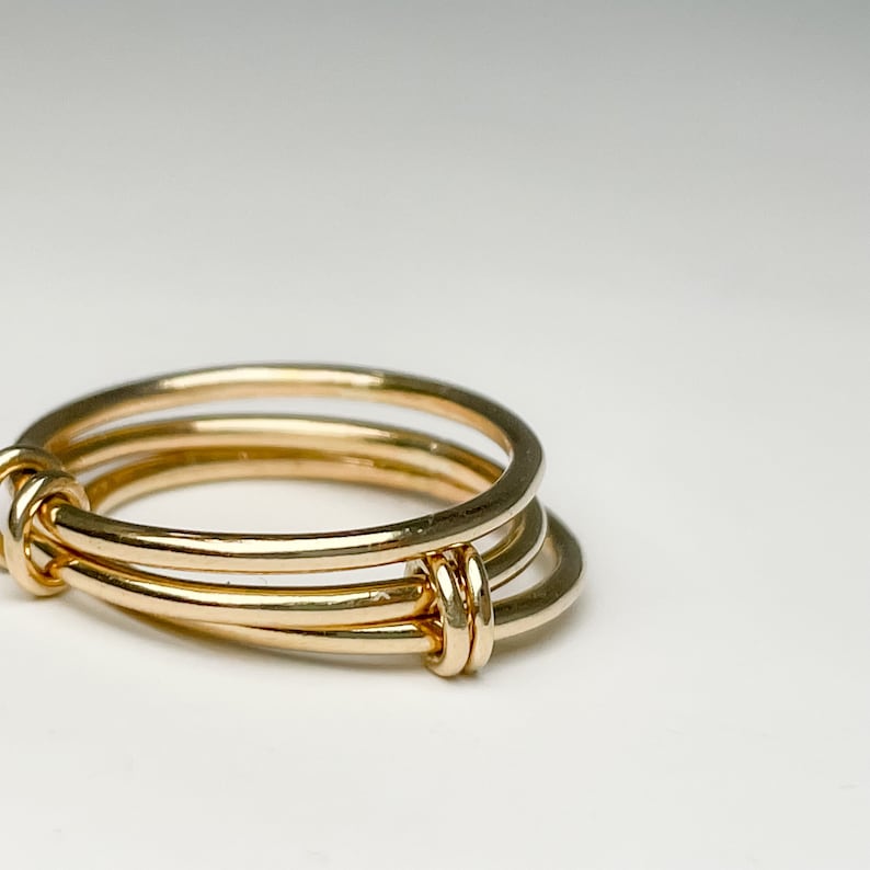 May include: A gold ring with three bands intertwined. The bands are smooth and polished.
