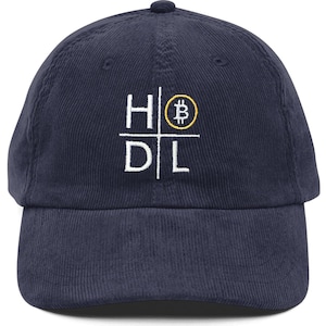 May include: Navy blue corduroy baseball cap with the white text "HODL" and a gold Bitcoin symbol. The cap has a curved brim and an adjustable strap at the back.