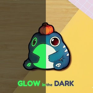 Peut inclure: Une créature de dessin animé bleue et verte avec une citrouille sur la tête. La créature a de grands yeux et un ventre blanc. Le texte "GLOW in the DARK" est au bas de l'image.