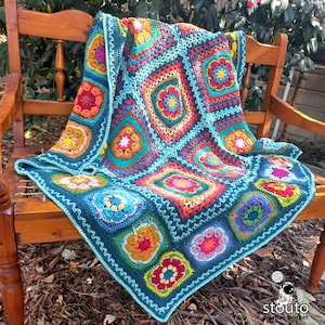 May include: A colourful crochet blanket with a floral pattern in shades of blue, green, red, orange, and yellow. The blanket is made of squares with a border of teal blue and white.