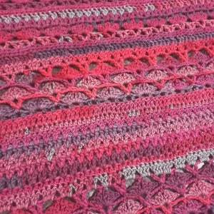 Close up image of crochet poncho image, stitch variations and combinations in red, silver, dark purple, maroon and crimson colors, pebbeld fliwer crochet stitches along with Vstitches and double crochet stitches