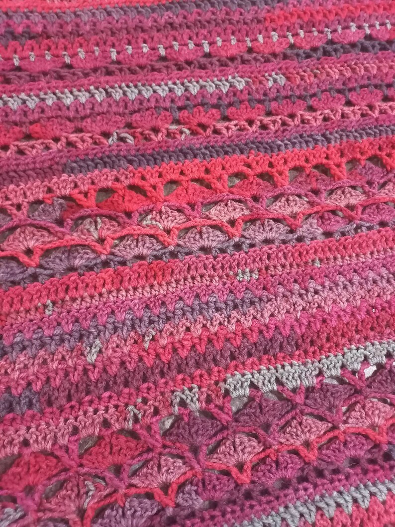 Close up image of crochet poncho image, stitch variations and combinations in red, silver, dark purple, maroon and crimson colors, pebbeld fliwer crochet stitches along with Vstitches and double crochet stitches