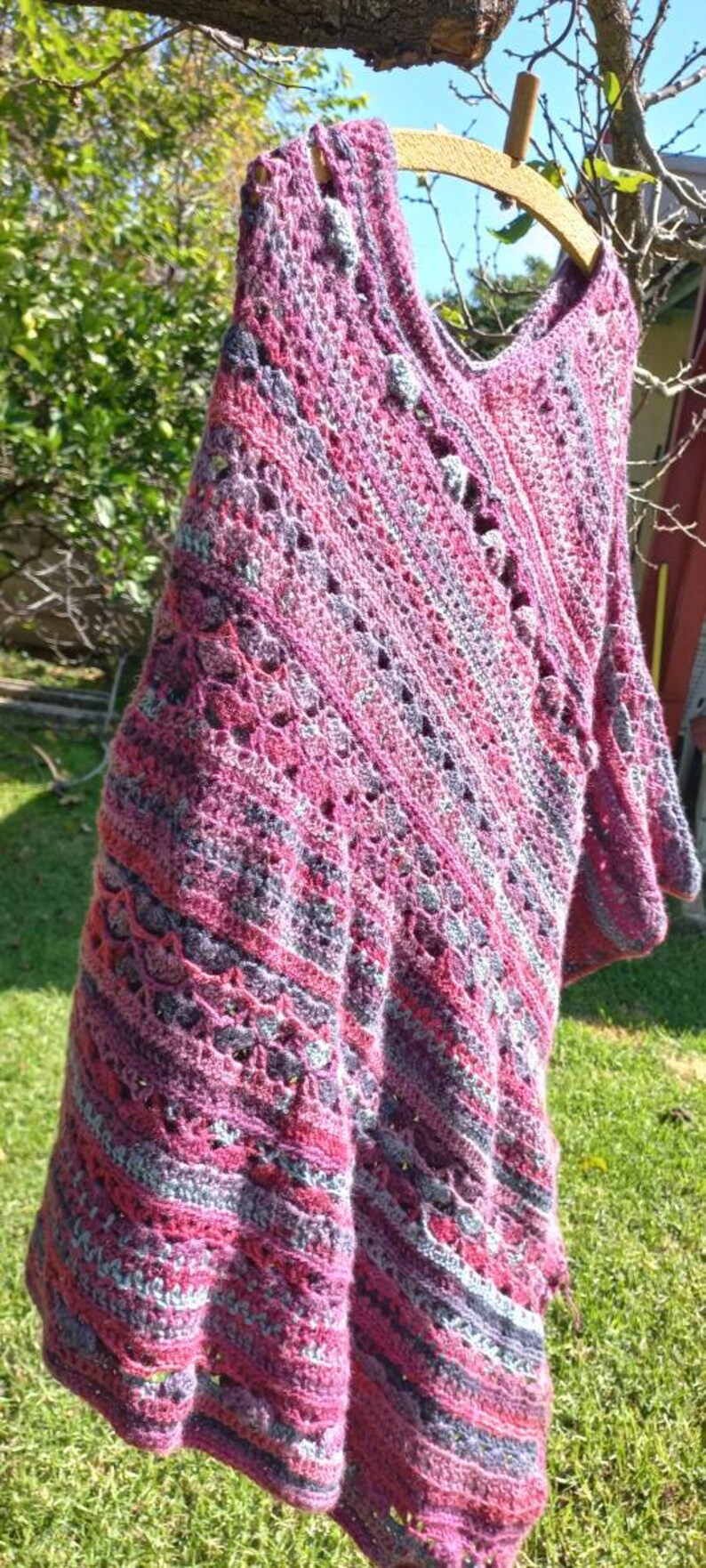 Sun kissed textured crochet poncho viewed from the side, draped on wooden coat hanger, shows the lined beauty of the variation of crochet stitches used in pattern