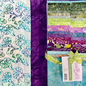 May include: A collection of colorful batik fabric squares, tied with a green ribbon. The fabric features a variety of patterns and colors, including shades of blue, green, purple, and yellow. A separate piece of fabric with a white background and blue and green floral design is also visible.