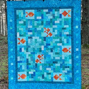 May include: A blue and green patchwork quilt with a fish design. The quilt is made up of many different squares of fabric, each with a different pattern. The fish are orange and white and are scattered throughout the quilt.