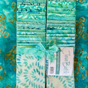May include: Stacks of batik fabric in shades of teal, turquoise, and green, tied with a matching ribbon. The fabric has various patterns, including floral and abstract designs. A tag reads "Java Batik" from Maywood Studio.