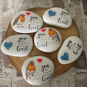 May include: White painted stones with robin bird illustrations, red hearts, and the text "You are always in my heart." The stones are arranged on a wooden base. A thoughtful gift idea for loved ones.