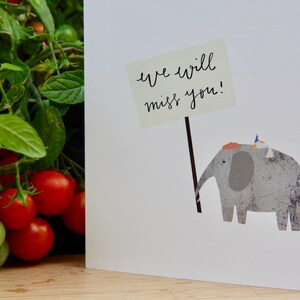 May include: A white card with a gray elephant holding a sign that says "We will miss you!" A small bird is perched on the elephant's back.