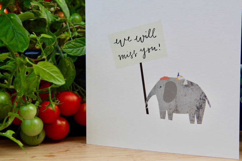 May include: A white card with a gray elephant holding a sign that says "We will miss you!" A small bird is perched on the elephant's back.