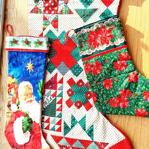 May include: Three Christmas stockings with festive designs. One features Santa Claus, another has a patchwork pattern with red and green triangles, and the third showcases red poinsettias on a green background. Each has a loop for hanging.