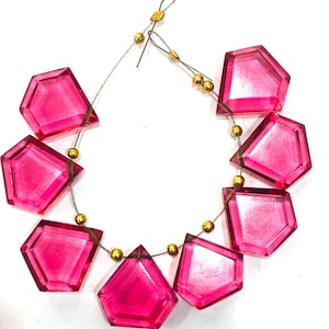 Puede incluir: Una hebra de cuentas de piedras preciosas facetadas de color rosa con detalles dorados. Las cuentas están enhebradas en un alambre plateado y tienen forma de diamante.