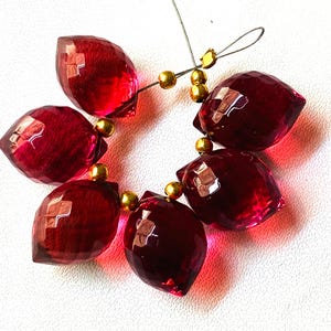 May include: A strand of six faceted, deep red gemstone beads with gold spacers. The beads are strung on a silver wire.