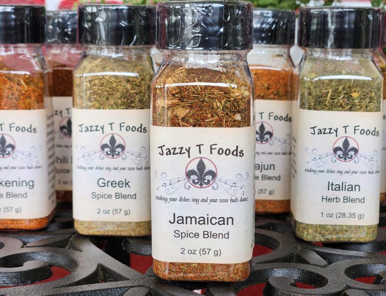 May include: Several glass spice jars with black lids, each labelled with a different spice blend name. The labels feature the "Jazzy T Foods" logo and include the weight of the contents in grams. The jars are filled with various herbs and spices.