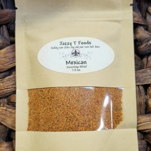 May include: A small brown paper pouch with a clear plastic window showing a brown and orange spice blend. The pouch has a white label with the text "Jazzy T Foods" and "Making your dishes sing and your taste buds dance". Below the text is a small black and white image of a fleur-de-lis. The label also says "Mexican Seasoning Blend 1.5 oz."