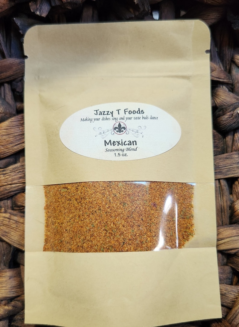 May include: A small brown paper pouch with a clear plastic window showing a brown and orange spice blend. The pouch has a white label with the text "Jazzy T Foods" and "Making your dishes sing and your taste buds dance". Below the text is a small black and white image of a fleur-de-lis. The label also says "Mexican Seasoning Blend 1.5 oz."