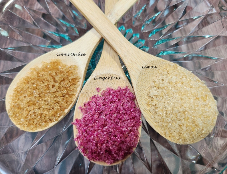 May include: Three wooden spoons filled with different colored sugar crystals. The spoons are labeled "Creme Brulee", "Dragonfruit", and "Lemon".