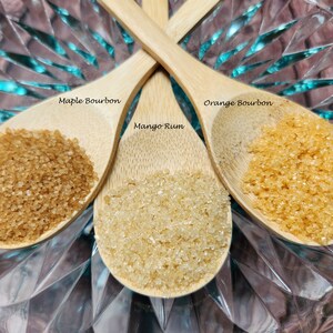 May include: Three wooden spoons filled with brown sugar. The spoons are labeled "Maple Bourbon", "Mango Rum", and "Orange Bourbon".