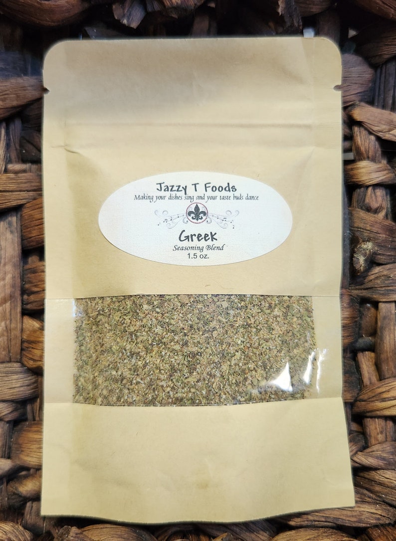 May include: A brown paper pouch with a clear plastic window showing a green Greek seasoning blend. The pouch has a white label with the text "Jazzy T Foods" and "Making your dishes sing and your taste buds dance". The label also has a white oval with the text "Greek Seasoning Blend 1.5 oz."