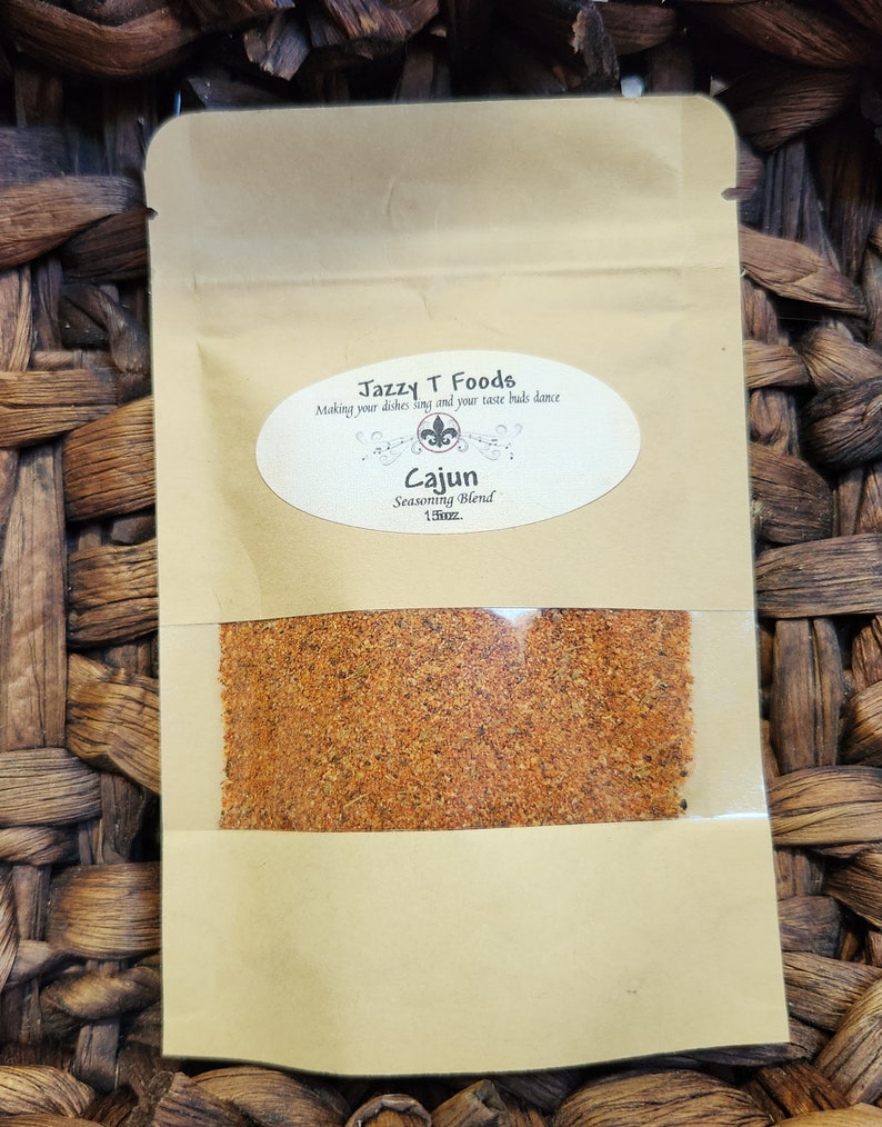 May include: A brown paper bag with a clear window showing a red and orange spice blend. The bag has a white label with the text "Jazzy T Foods" and "Making your dishes sing and your taste buds dance". The label also includes the text "Cajun Seasoning Blend 1.5oz."