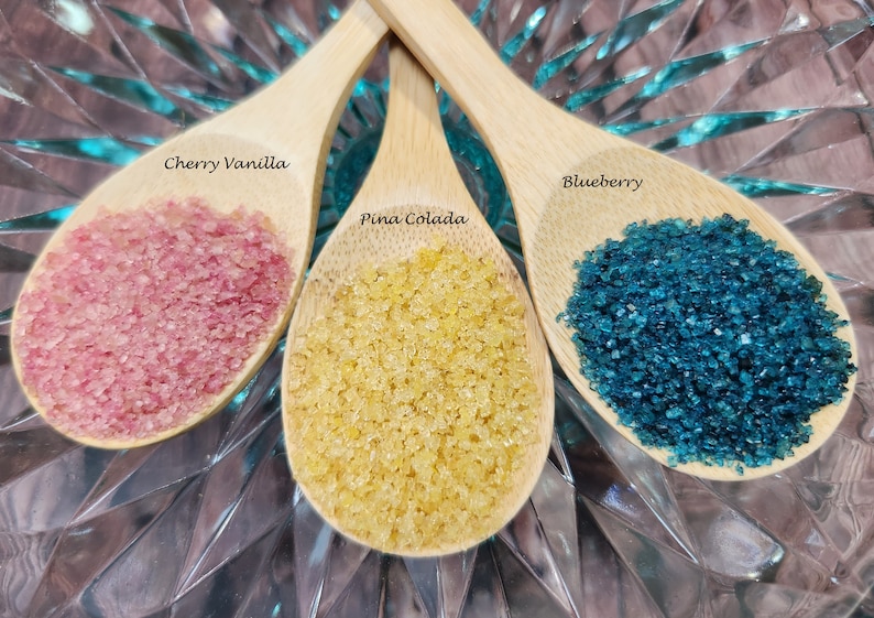 May include: Three wooden spoons filled with colorful sugar crystals. The spoons are labeled "Cherry Vanilla", "Pina Colada", and "Blueberry".