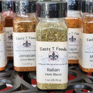 May include: A collection of glass spice jars with black lids, each with a white label. The labels read "Jazzy T Foods" and feature different spice blends, including "Italian Herb Blend". The Italian blend jar contains 28.35 g of herbs.
