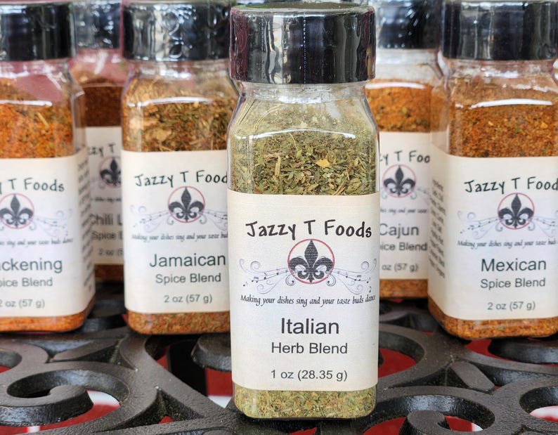 May include: A collection of glass spice jars with black lids, each with a white label. The labels read "Jazzy T Foods" and feature different spice blends, including "Italian Herb Blend". The Italian blend jar contains 28.35 g of herbs.