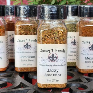 May include: A selection of spice blends in clear glass jars with black lids. Each jar features a label with the "Jazzy T Foods" logo and the spice blend name. The jars are 57 g each.