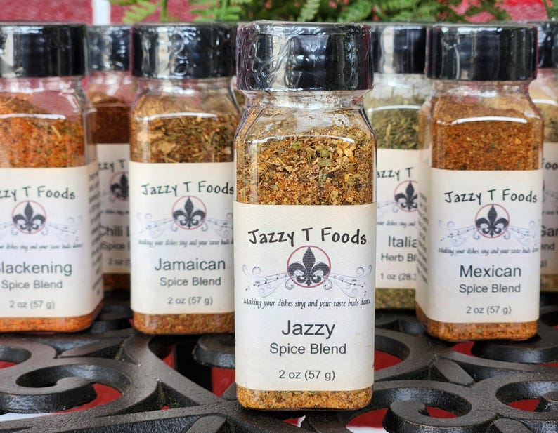 May include: A selection of spice blends in clear glass jars with black lids. Each jar features a label with the "Jazzy T Foods" logo and the spice blend name. The jars are 57 g each.