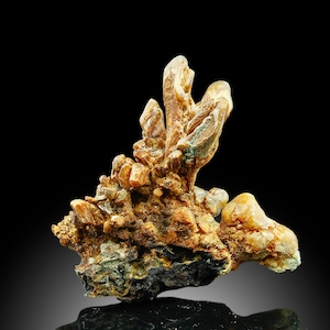 Peut inclure: Un amas de cristaux brun doré avec une surface rugueuse et texturée. Les cristaux sont disposés en une forme irrégulière et organique, ressemblant à une petite chaîne de montagnes. Les cristaux sont placés sur un fond noir.