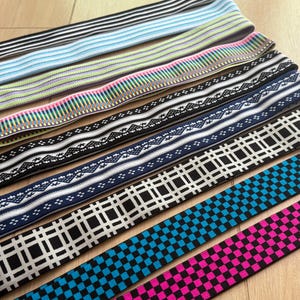 Op de afbeelding: Een verzameling elastische banden in verschillende patronen en kleuren. Ontwerpen omvatten strepen, geometrische vormen en bloemmotieven. Kleuren vari&euml;ren van zwart en wit tot blauw, roze en groen. De banden worden waarschijnlijk gebruikt voor naai- of knutselprojecten.