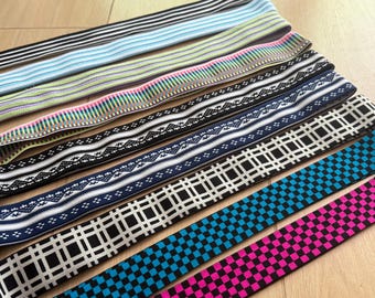 May include: A collection of elastic bands in various patterns and colors. Designs include stripes, geometric shapes, and floral motifs. Colors range from black and white to blue, pink, and green. The bands are likely used for sewing or crafting projects.