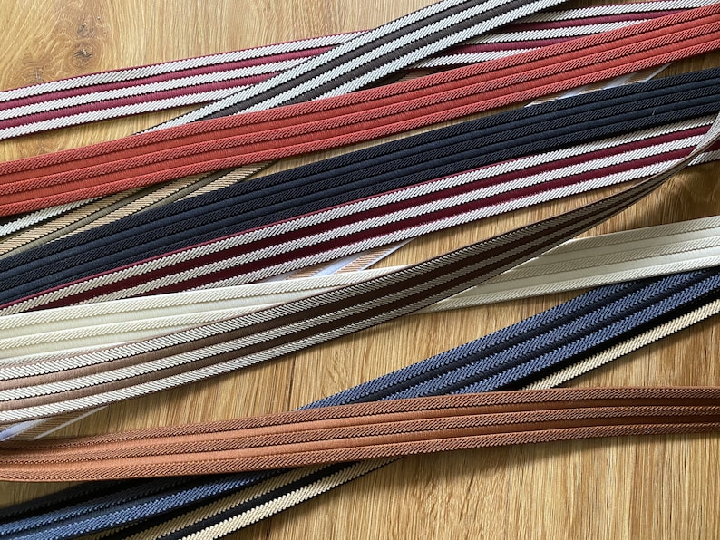 May include: Assortment of striped fabric trim in various colors, including red, brown, beige, white, and blue. The trim has a woven texture and is suitable for sewing and crafting projects.