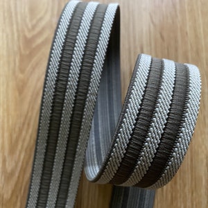 May include: Brown and white striped woven trim with a textured surface. The trim is approximately 1 inch wide.