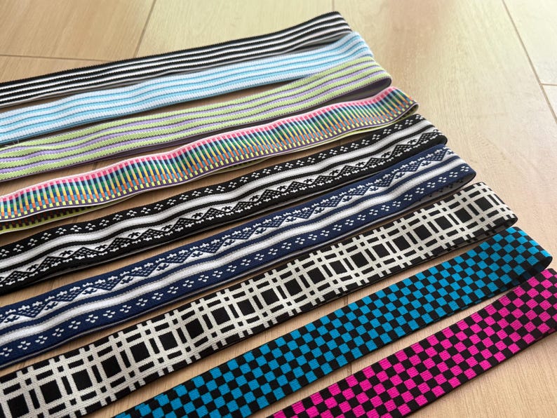 Op de afbeelding: Assortiment elastische banden in diverse kleuren en patronen. Ontwerpen omvatten strepen, geometrische vormen en bloemmotieven. Kleuren vari&euml;ren van zwart en wit tot blauw, roze en groen. De banden zijn waarschijnlijk voor naai- of knutselprojecten.