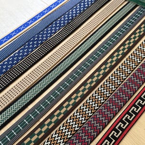 Op de afbeelding: Een collectie van tien parallelle stoffen linten met diverse patronen, waaronder blauw met witte kruisen, marineblauw met witte ankers, zwart met witte stippen, beige, groen met witte lijnen, groen geblokt en rood met witte geometrische ontwerpen.