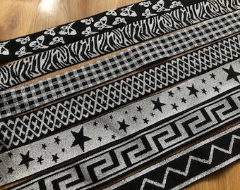 Puede incluir: Una colección de seis cintas elásticas negras y plateadas con diferentes patrones, incluyendo mariposas, rayas de cebra, cuadros, estrellas, llave griega y zigzags.