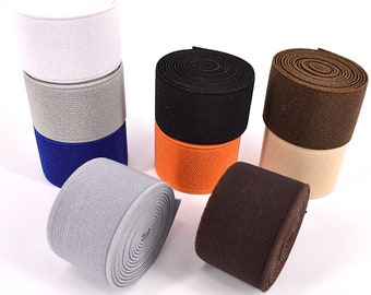 May include: Assortment of elastic bands in various colors, including white, gray, blue, orange, brown, and beige. The elastic bands are rolled up and stacked on a white surface.