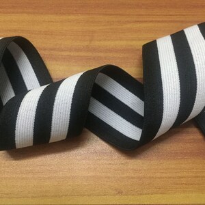 May include: Black and white striped elastic trim with a woven texture. The trim is approximately 1 inch wide.