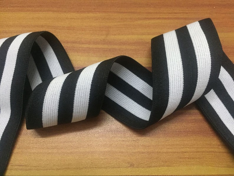 May include: Black and white striped elastic trim with a woven texture. The trim is approximately 1 inch wide.