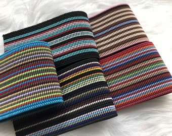 May include: Four rolls of striped elastic trim in various colors, including black, brown, red, and blue. The trim is made of a woven fabric with a textured surface.