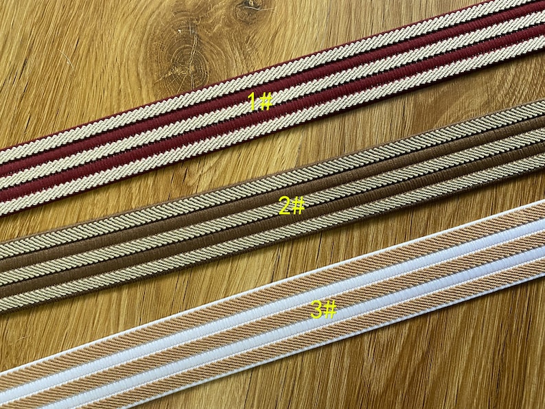 May include: Three different types of elastic trim with two white stripes on a brown background. The trim is shown on a wooden surface. The trim is labeled 1#, 2#, and 3#.