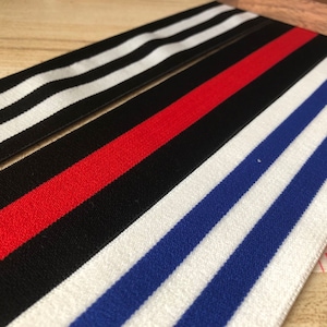May include: Three different striped elastic bands. The first band is black and white, the second band is black, red, and white, and the third band is white, blue, and white.