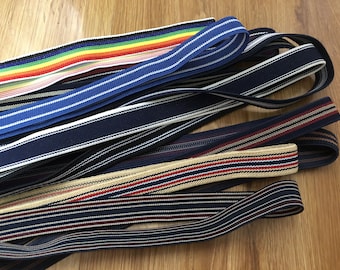 May include: A collection of striped elastic trim in various colors, including navy blue, white, red, beige, and rainbow. The trim is made of woven fabric and has a stretchy texture.
