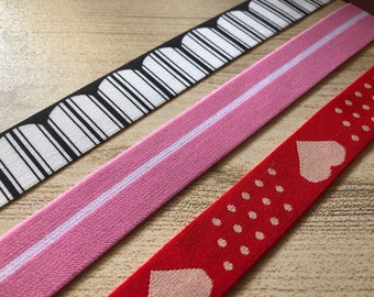 Könnte beinhalten: Drei verschiedene Arten von elastischem Besatz mit verschiedenen Mustern. Der erste Besatz ist schwarz-weiß mit einem geometrischen Muster. Der zweite Besatz ist rosa mit einem weißen Streifen. Der dritte Besatz ist rot mit einem weißen Herzen und weißen Punkten.
