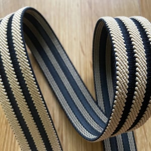 May include: Black and beige striped elastic band. The band is woven with a textured pattern.