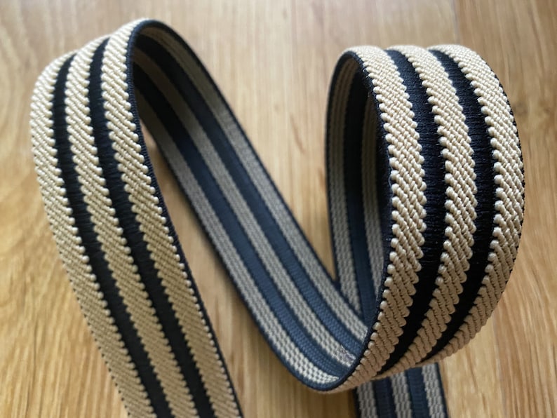 May include: Black and beige striped elastic band. The band is woven with a textured pattern.